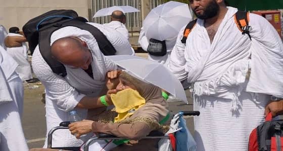 بالصور.. لقطات مؤثرة لحاج يخفف عن والدته المسنة حرارة الشمس الحارقة